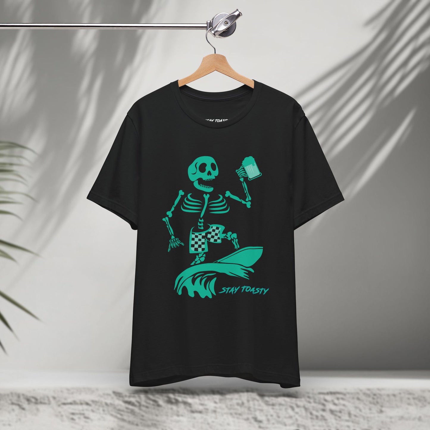 Black t-shirt with a skeleton surfer design holding a beer and 'Stay Toasty' text on a hanger