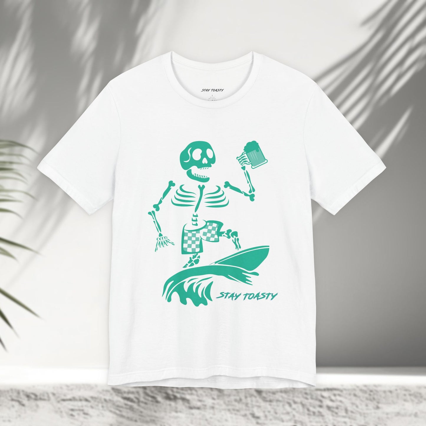 White t-shirt with a skeleton surfer design holding a beer and 'Stay Toasty' text 