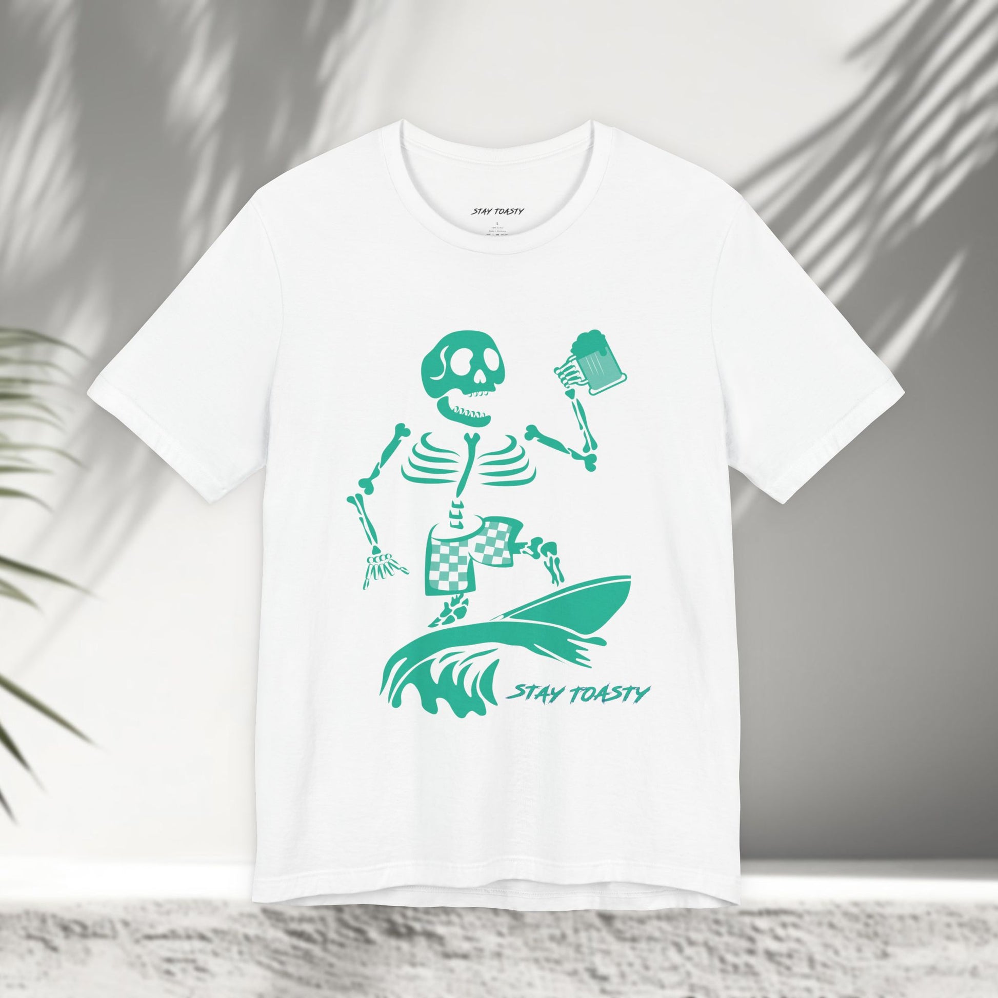 White t-shirt with a skeleton surfer design holding a beer and 'Stay Toasty' text 