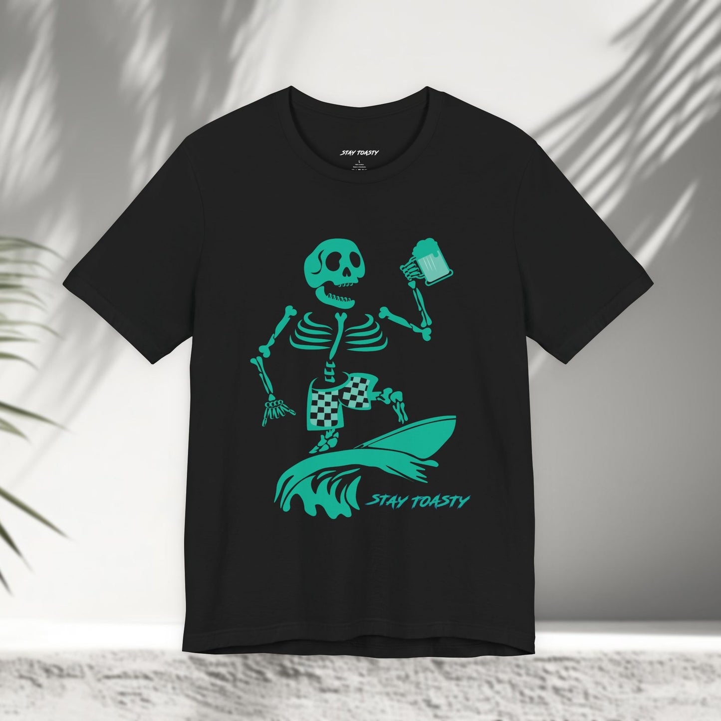 Black t-shirt with a skeleton surfer design holding a beer and 'Stay Toasty' text 