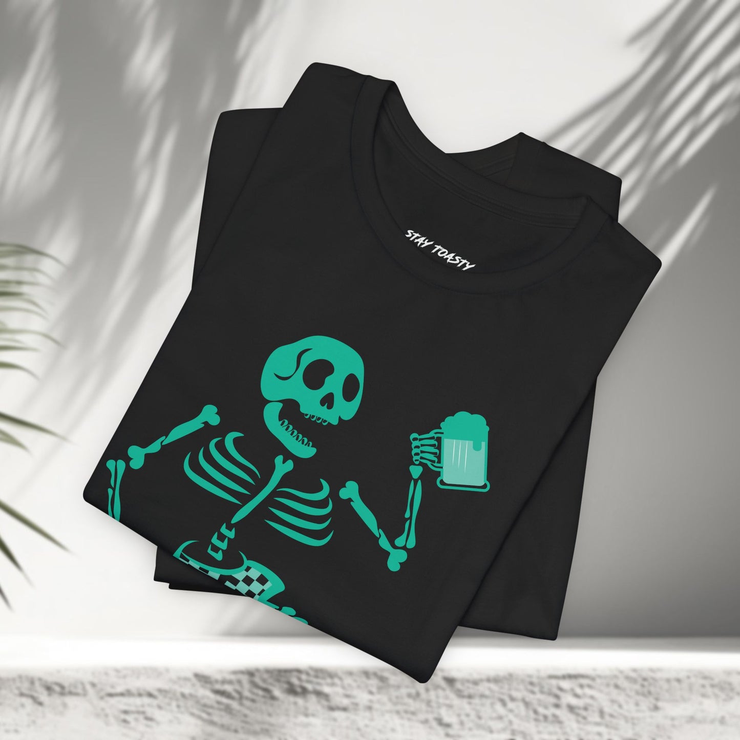 Black t-shirt with a skeleton surfer design holding a beer and 'Stay Toasty' text shown folded