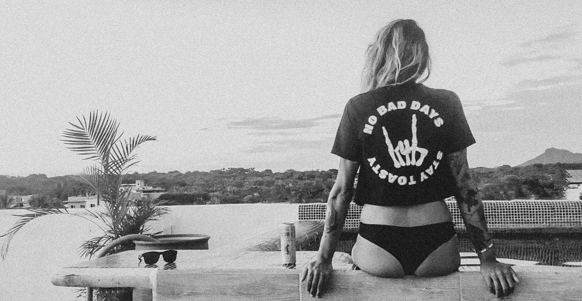 Person wearing a black t-shirt with 'No Bad Days' text and a white graphic, sitting on a pool rooftop.