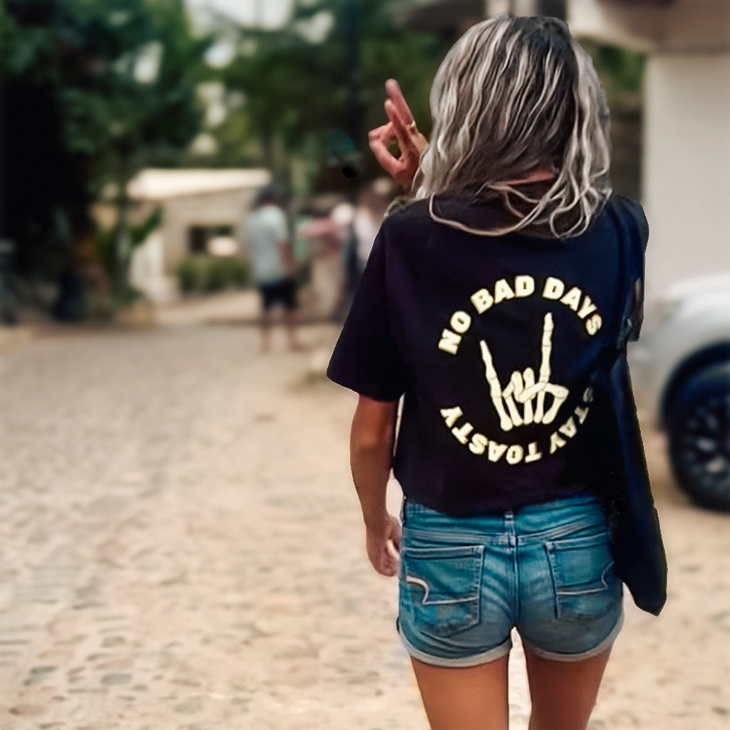 A woman walking down a street, seen from behind, wearing a black crop top with the text ‘No Bad Days’ and a skeleton hand graphic on the back.