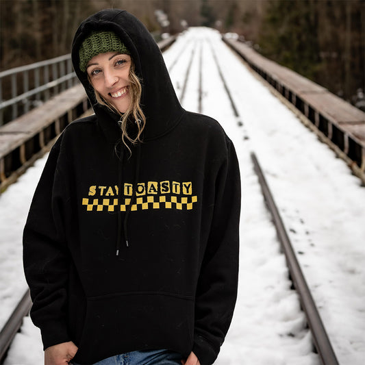 Person wearing a black hoodie with yellow 'Stay Toasty' text and checkers on snow-covered tracks