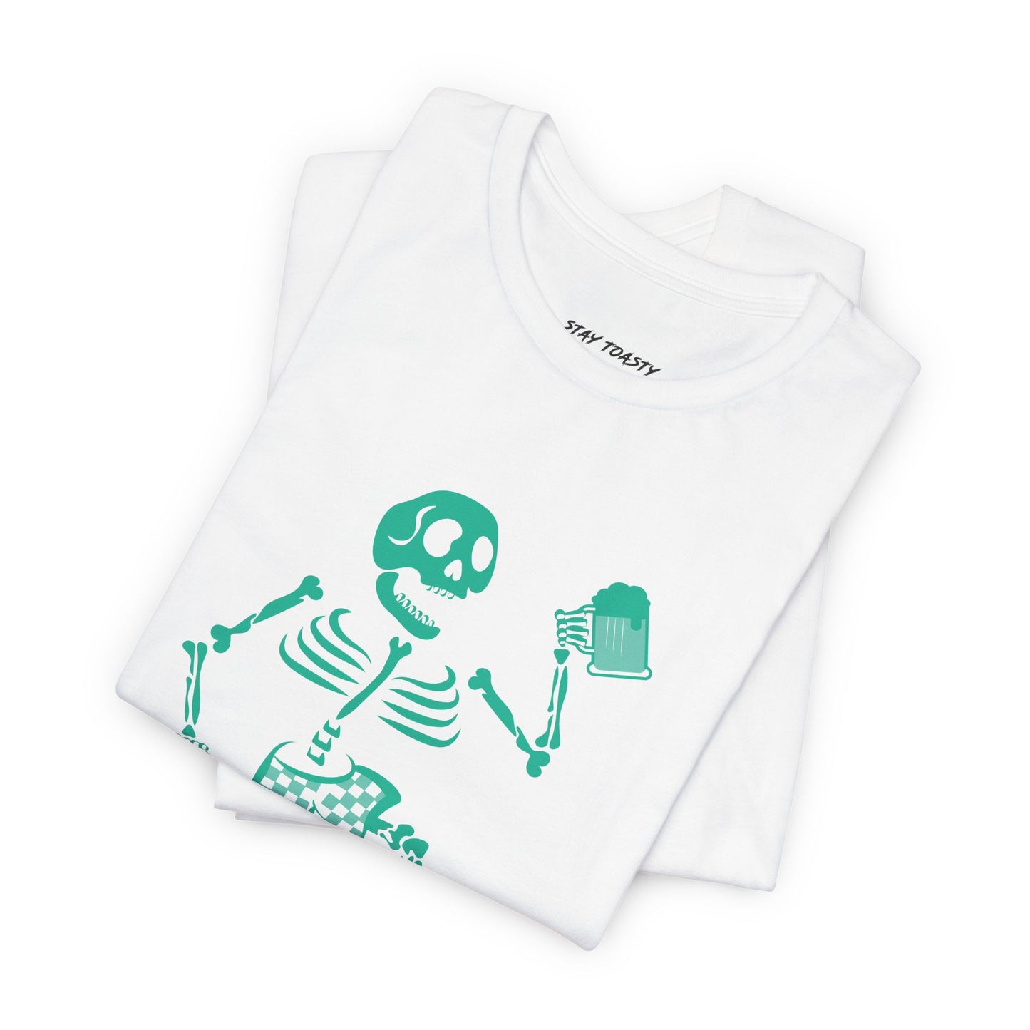 A folded white t-shirt featuring a bright teal-green skeleton graphic holding a beer, with the brand name 'stay toasty' 