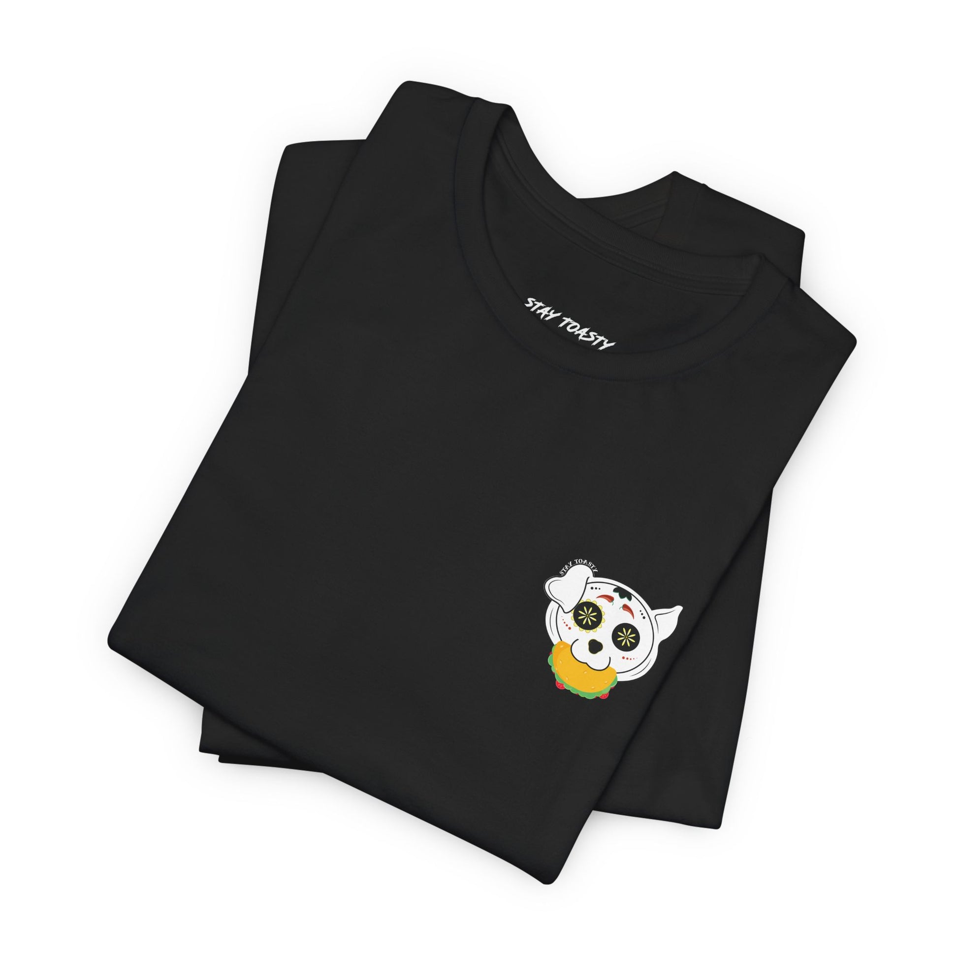 Folded black tee with front chest graphic of a sugar skull dog with a taco in his mouth. Design by Stay Toasty.